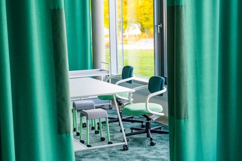 Table and chairs next to large windows surrounded by green curtains