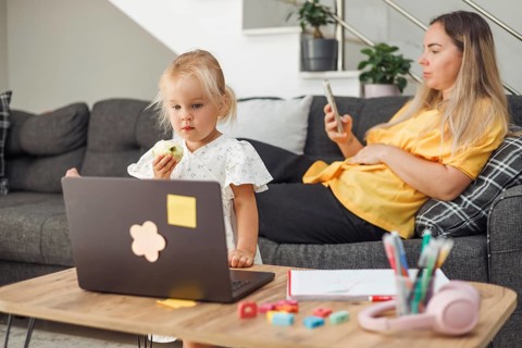 Young blond European girl eating sandwich with laptop on table. Pregnant blond European woman
