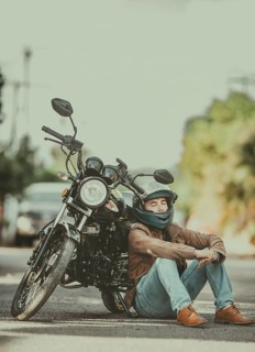 Male motorcyclist in jacket sitting leaning to his motorcycle on the road