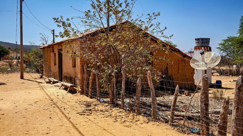 Old house with satellite dish and wooden fence in sunny, dry surroundings, houses in a village in