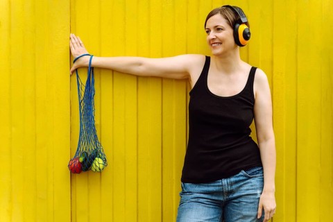 Smiling woman with yellow headphones carrying eco grocery bag on yellow, Woman wearing headphones