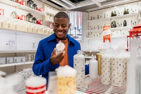 A young African man smiles while shopping in a store filled with various decorative candles. The