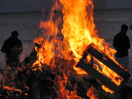 Easter bonfire, bonfire on the beach, bright flames and burning wood, dark silhouettes of tourists