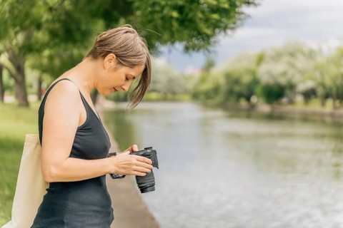 Woman 40s reviewing travel photos on camera by urban river, Woman examining her camera by a