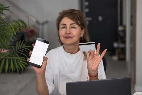 Mature pretty woman using credit card for online payment at home. Successful middle aged woman