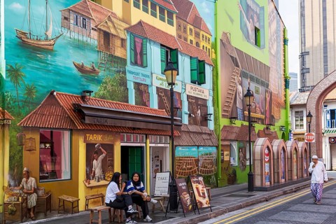 People sitting outside of a cafe by contemporary street art of the Muscat Street Murals, Kampong