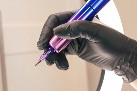 Close-up of a gloved hand holding a purple and blue tattoo machine