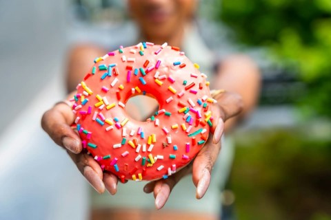 Hands presenting a delicious vibrant doughnut topped with bright pink icing and colorful sprinkles,