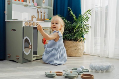 Young child smiles while playing with kitchen toys in well-decorated, light-filled room. The