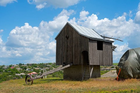 Wooden windmill in a field under blue sky with clouds in the background, surrounded by rural