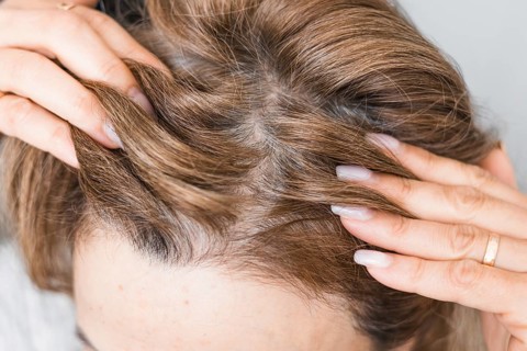 Mature middle-aged caucasian woman touching her gray, silver roots hair close-up on gray tiles