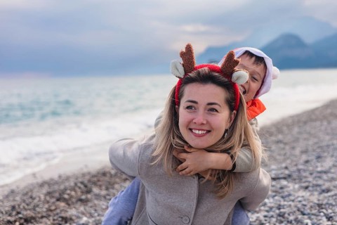 A young Caucasian woman with long blonde hair wears reindeer antlers. A young boy with brown hair