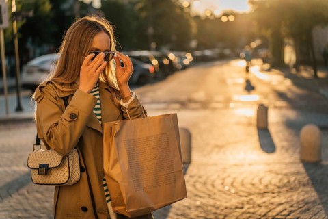 A woman walks around the city after shopping at sunset with a paper bag, Woman wearing sunglasses
