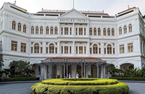 White colonial facade of the 1887 Raffles Hotel beside its circular lawn with staff at the