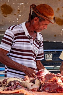 Man in traditional clothing cuts up concentrated meat on a slaughter table, market scene in a small
