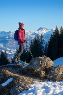 Nice and active senior woman snowshoeing in in the snow covered Allgaue alps above the valley of