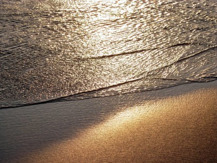 Close-up of an ocean coast in the golden light of the setting sun, soft waves rolling on the wet,