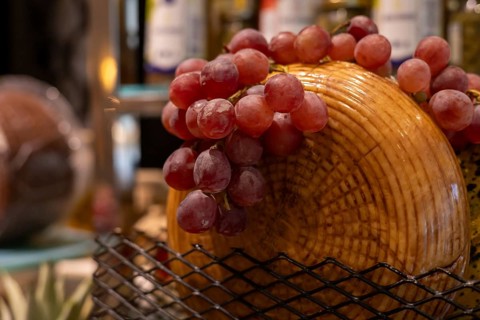 A basket filled with fresh red grapes sits atop a wooden cheese board. The cozy atmosphere enhances