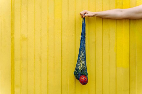 Eco-friendly mesh tote with fresh veggies isolated on yellow background, A hand holding a blue net