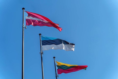 Latvian, Estonian and Lithuanian flags on flagpoles against blue clear sky, Three national flags of