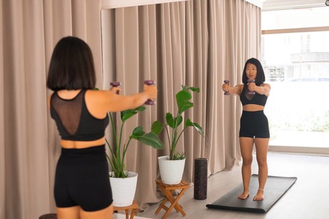 A woman facing the mirror holding dumbbells straight ahead during a workout