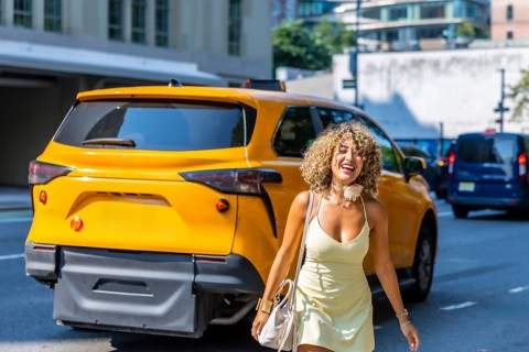 Cheerful woman with curly hair walking confidently on a manhattan street, passing a yellow taxi,
