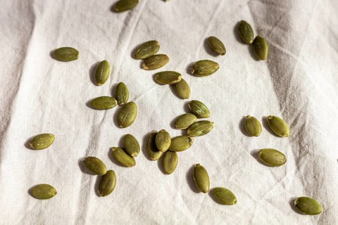 Green pumpkin seeds scattered on a light fabric background. The seeds are raw and unroasted,