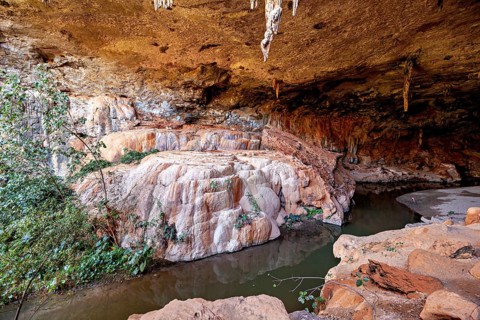 Rock formations and hanging stalactites in a cave with vegetation-rich surroundings, The Gruta do