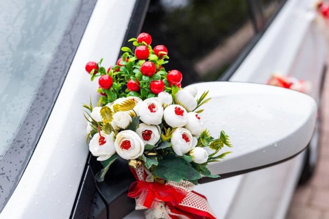 A white car decorated with flowers and ribbons. The flowers are red and white, attached to the side