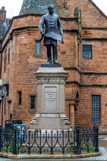 Blackened bronze statue of shipbuilder Sir William Pearce holding a design plan, standing at Govan