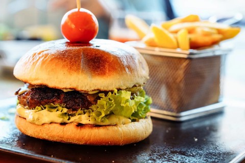 Focus on the foreground burger and fries, A close-up of a gourmet burger with lettuce and a cherry