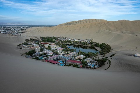 The oasis, Laguna Huacachina with a small lake and houses surrounded by sand dunes in the Ica