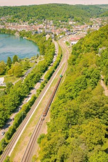 River bank with railway line and surrounding forest, city in the background, summery atmosphere,