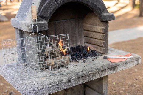 A stone barbecue grill with burning charcoal and flames. A metal grill rack is placed on top. The