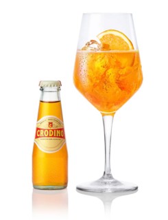 Crodino on ice cube cubes in a wine glass, half an orange slice as garnish, next to a bottle of