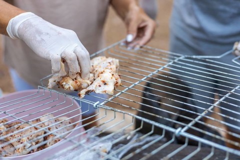 Hands placing marinated chicken pieces on a grill. The scene shows a close-up of food preparation