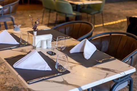 A modern restaurant table set for dining. The table features a marble top with neatly folded