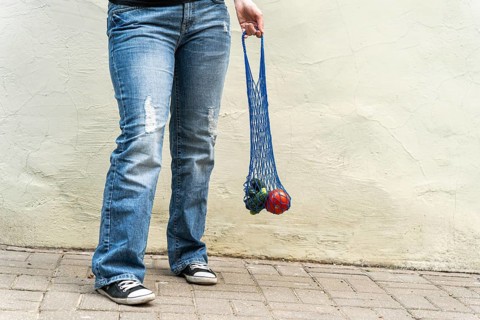 Urban grocery run: blue mesh bag with veggies in denim and sneakers POV, Person holding a blue mesh