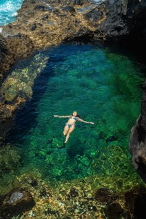 Woman in a blue bikini enjoying vacation, floating effortlessly on her back in a volcanic natural