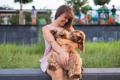 A woman playfully holds her dog, surrounded by vibrant park scenery