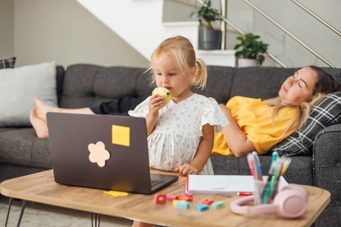 Young blond European girl eating an apple near a laptop on a table. Relaxed European woman with