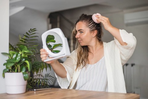 Woman, aking sculp head massage and applying hair product while looking in a mirror in a modern