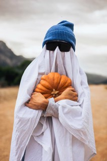 Person dressed as a ghost holding a pumpkin outdoors during Halloween celebration. Homemade