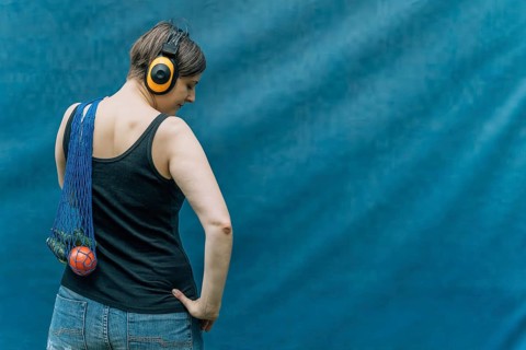 Woman with yellow headphones carrying mesh grocery bag, back view on blue, A woman with headphones,
