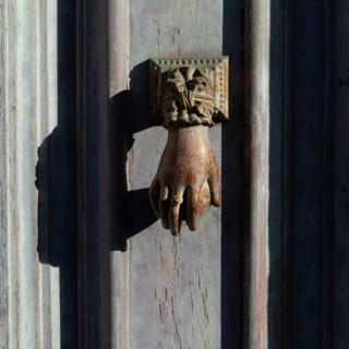 Antique hand door knocker on weathered wooden door