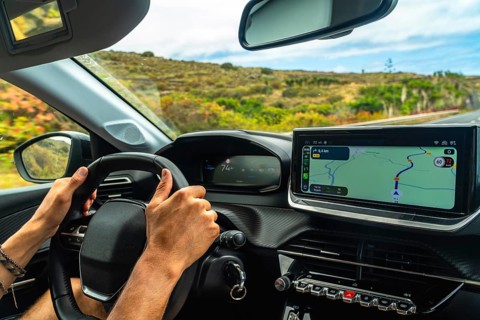 Person driving a modern car on a scenic road, using an infotainment system with gps navigation to