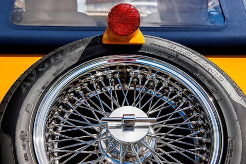 Chrome wire wheel and red tail light on a yellow and blue classic sports car