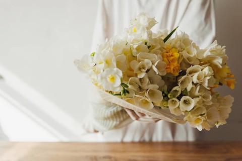 Florist in white outfit stands on white background and holds bouquet of white and yellow