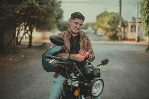 Young motorcyclist suffering from arthritis pain on the road. Motorcyclist with hand pain on the