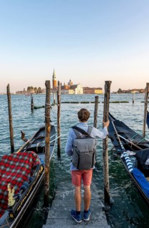 Young man at a boat dock for Venetian gondolas in St. Mark's Square, tourist enjoying the evening,